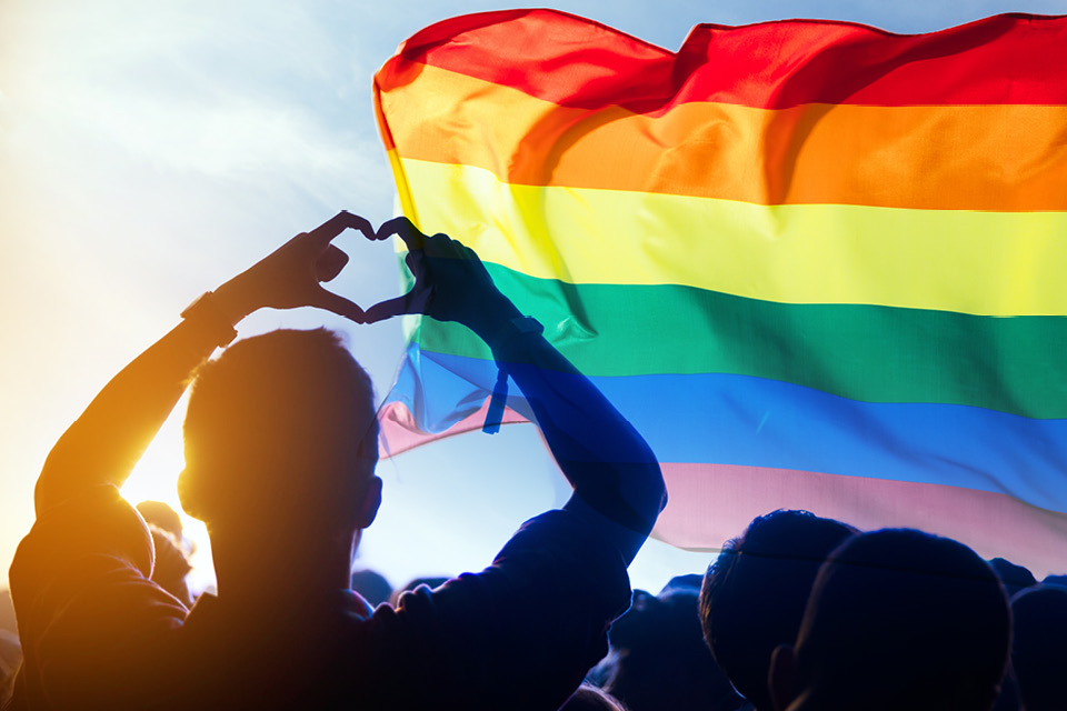LGBT flag with a silhouette of a person making a love heart with their hands 